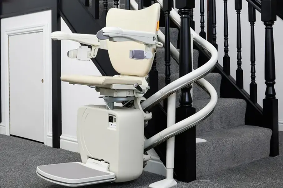 A Freedom Stairlifts Curved Stairlift 2 with twin tracks in a light coloured upholstery in an open positon at the foot of the stairs, installed internally on the curve of the stairs.